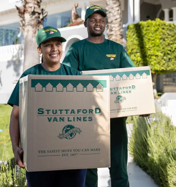 Two Stuttaford Van Lines staff in uniform carrying moving boxes out of a house.